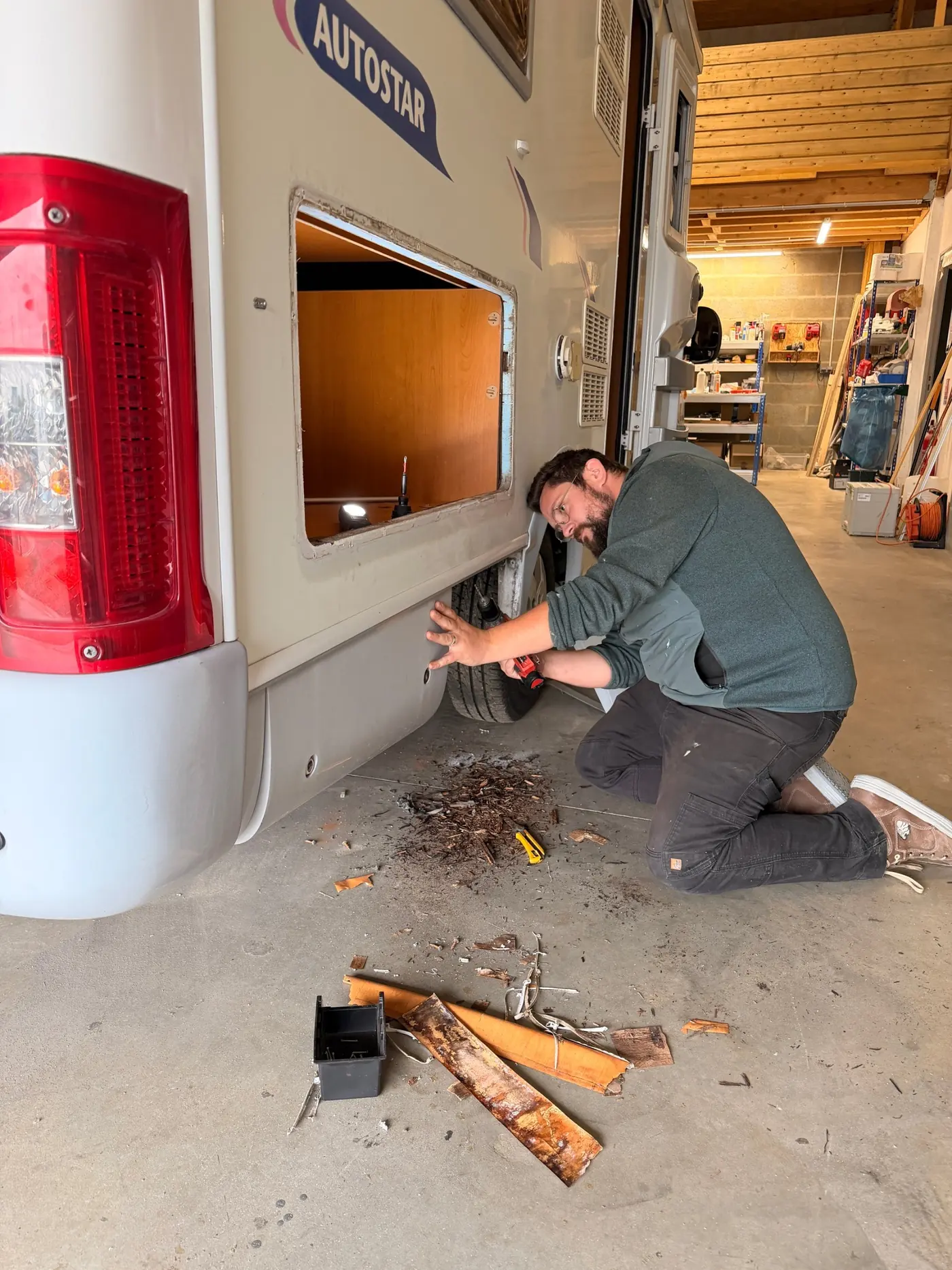 Quentin, à genoux dans l'atelier, en train de réparer le bas de caisse d'un camping-car