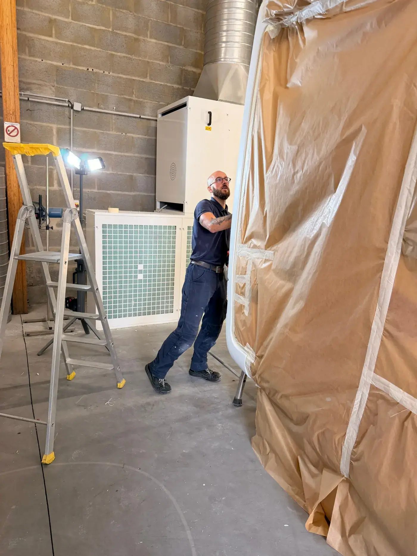 Simon, carrossier-peintre, au travail près d'un véhicule masqué dans la cabine de peinture